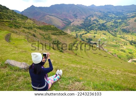 Female traveler taking photos from the mountain slope of Pisac archaeological park, Sacred valley of the Incas, Cusco region, Peru