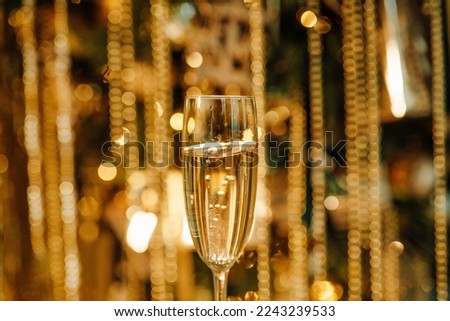Flute glasses with bubbly wine at sparkling bokeh yellowish golden sequin garlands blaze. Bright falling gold glitter ribbons backdrop glittering twinkle decoration for celebrating luxury party