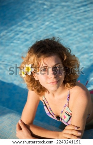 portrait of beautiful happy young woman, slender teenage girl, with curly hair, is relaxing in the water of the pool. Enjoy the moment, rest . Sunbathing with pleasure, cheers holidays