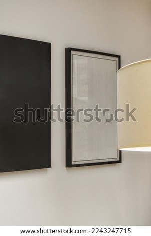 a black and white painting hangs on the wall next to a lamp in a room with two framed art pieces