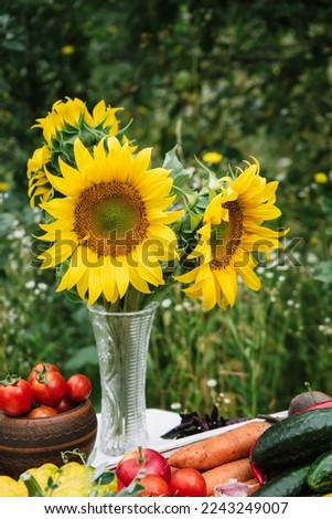 a bouquet of sunflowers on a table with an autumn harvest of vegetables and fruits on a natural green background