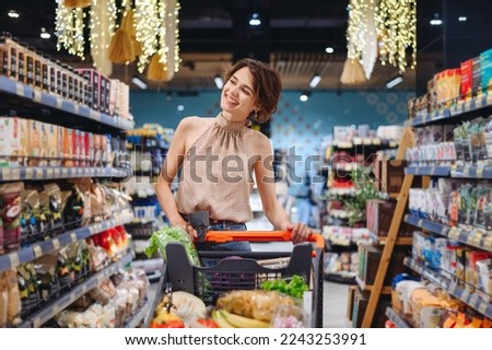 Young happy smiling woman 20s wearing casual clothes shopping at supermaket store buy choosing pasta products browsing with grocery cart inside hypermarket People purchasing gastronomy food concept Royalty-Free Stock Photo #2243253991