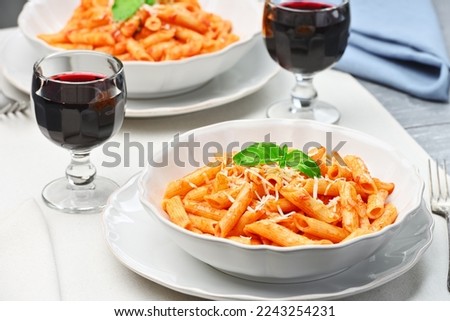 Plates of All'Arrabbiata penne pasta with cheese and basil, as well as glasses of red wine. Studio shot from a high angle.