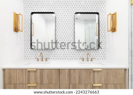 A beautiful bathroom with a floating wood vanity cabinet, gold faucet and lights, mosaic tile wall, and rectangular mirrors. Royalty-Free Stock Photo #2243276663