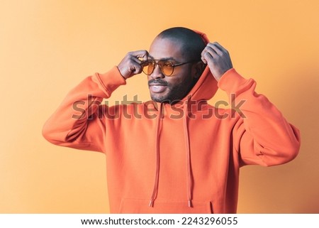 A  man peers over the top of his glasses, The black boy is wearing an orange sweatshirt,orange outdoor background.