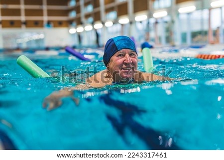 Side view of older adult man swimming with a pool noodle . High quality photo Royalty-Free Stock Photo #2243317461