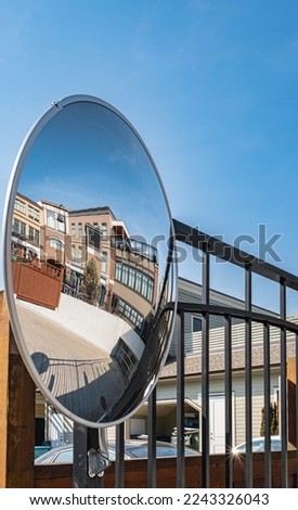 Outdoor convex safety mirror hanging on wall with reflection of an urban roadside view by residential apartment buildings. Round mirror on a post to help cornering transport. Nobody, street photo