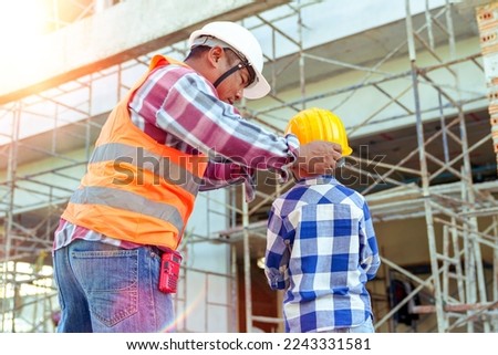 Male contractor holding boy's hand standing looking at building under construction, father taking son to look at his construction site, low view from behind, father and son holding hands. Royalty-Free Stock Photo #2243331581