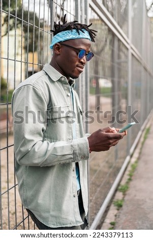 Young and cool black man standing in a fence and using his cellphone.