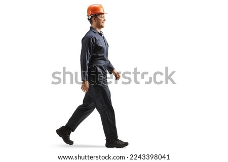 Full length profile shot of a factory worker wearing a helmet and uniform and walking isolated on white background