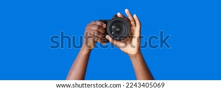 Hands of African-American photographer with camera on blue background