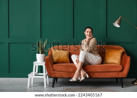 Young woman sitting on red sofa near green wall Royalty-Free Stock Photo #2243405167
