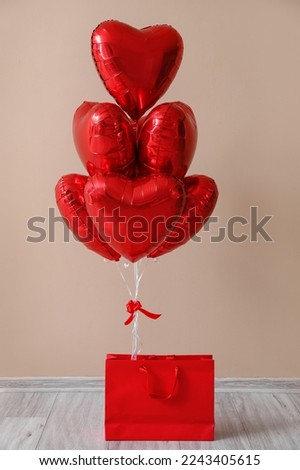 Shopping bag with heart-shaped balloons for Valentine's Day near beige wall