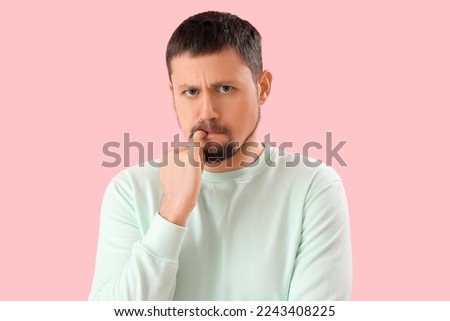 Handsome man biting nails on pink background, closeup