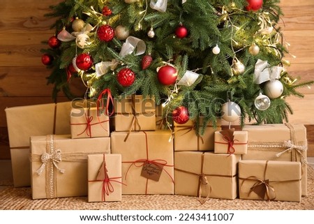 Gifts under glowing Christmas tree near wooden wall