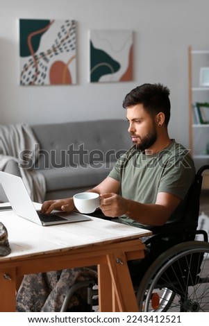 Soldier in wheelchair with cup of coffee using laptop at home