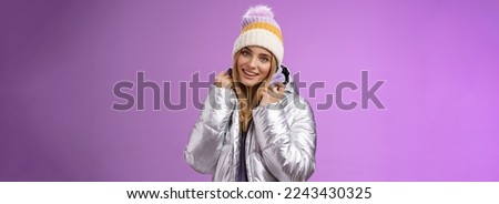 Tender feminine gentle blond girlfriend posing boyfriend take pictures ski resort holiday wearing glittering stylish jacket winter hat standing pleased purple background smiling delighted.