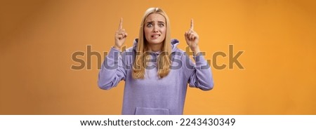 Worried perplexed unsure cute blond woman presenting project standing awkward afraid humiliation crining scared pointing up raised index finger waiting reply nervously, orange background.