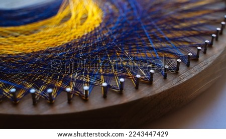 Colored thread mandala on a wooden board with nails. Mandala Moon Harmony Sun esotericism and psychology pictures from yellow and blue silk threads.