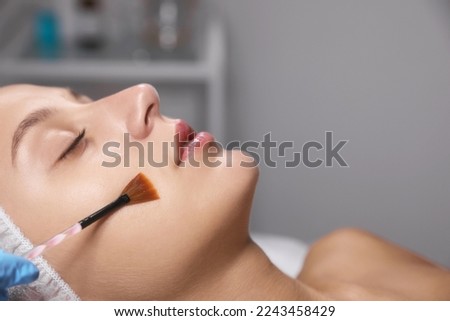 Cosmetologist applying chemical peel product on client's face in salon Royalty-Free Stock Photo #2243458429