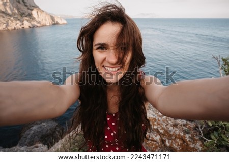 Selfie-portrait of a young woman against the background of the sea at the cliff. The girl smiles at the camera. The concept of tourism, recreation