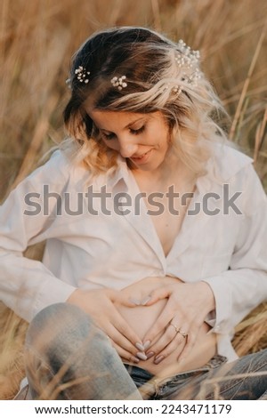 A picture of a happy future young mother- a woman in white clothes with a large pregnant belly against a natural landscape. The concept of pregnancy, motherhood. Third trimester