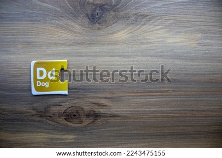 Yellow knowledge puzzle with letter d and dog lettering placed on left of wooden background.