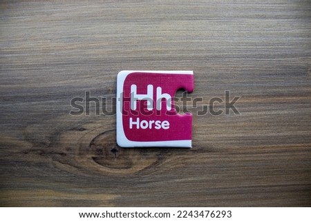 Pink knowledge puzzle with horse lettering and letter h placed on wooden background.