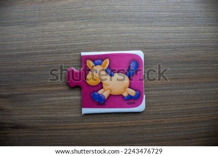 Pink knowledge puzzle with a picture of a running horse placed on a wooden background.