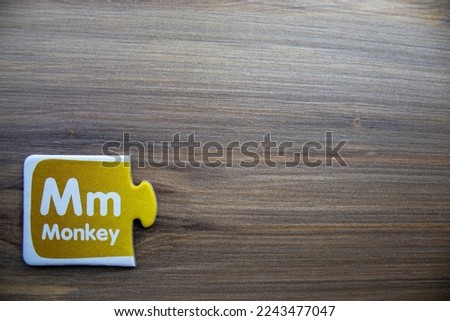 Yellow knowledge puzzle with the letter m and monkey writing on it, placed on the left of a wooden background.