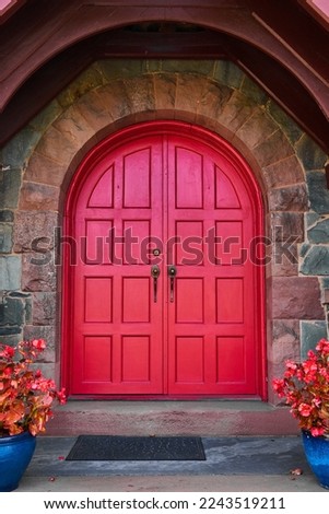 Stunning vibrant red arched double doors with stone arch and pair of red plants in blue pots Royalty-Free Stock Photo #2243519211