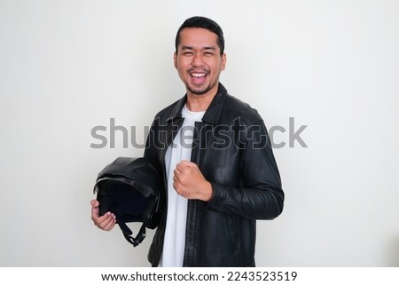 Asian man wearing black leather jacket holding motorcycle helmet with excited expression Royalty-Free Stock Photo #2243523519