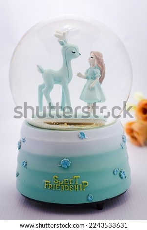 A lovely snow globe with a little girl and a deer in it, with an aqua blue base that has the words "sweet friendship" on it. 