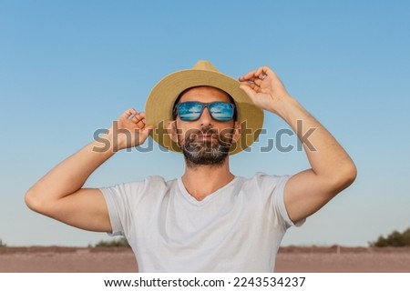 Hispanic man with beard, sunglasses and white t-shirt, adjusting his hat