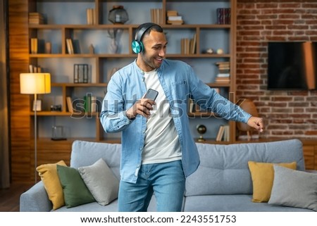 Guy singing song holding phone listening to music online wearing headphones dancing and having fun at home. Music lover concept