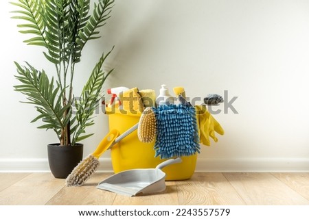 Brushes, bottles with cleaning liquids, sponges, rag and yellow rubber gloves on white background. Cleaning supplies in the yellow bucket on the wooden floor. Cleaning company service advertisement Royalty-Free Stock Photo #2243557579