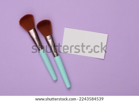 White Blank business card for branding and makeup brushes on purple background. Beauty concept. Top view