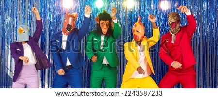 Cheerful funny eccentric young people with heads of different animals are dancing and having fun together. People in funny fancy rubber carnival masks and colorful suits on shiny background at party.