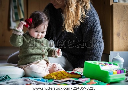 adorable baby playing on a play rug, next to her mother, holding her red socks instead of her toys in front of her.Real home environment