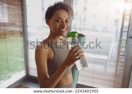 Woman drink water and holding rolled fitness mat after working out at home 
