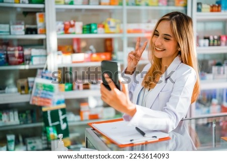 asian female pharmacist using mobile phone for selfie with v-sign hand gesture while working in pharmacy