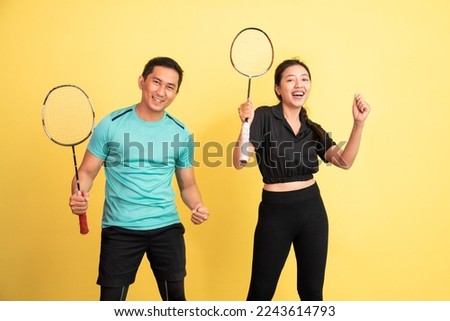 excited women and men standing holding rackets on yellow background