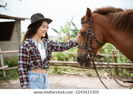 woman in cowboy hat stroking the head of a horse at the ranch