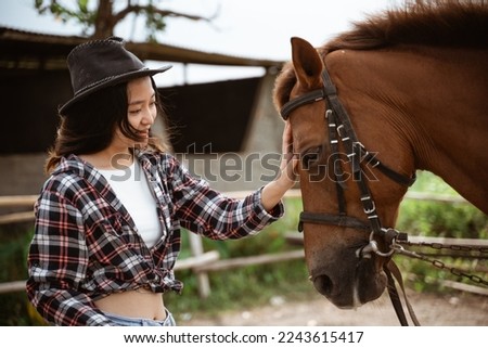woman in cowboy hat stroking the head of a horse at the ranch