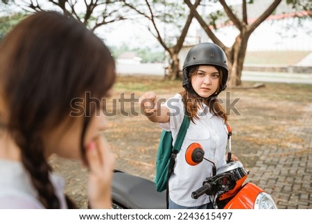 Student girl riding motorbike wearing helmet pointing finger when angry at her friend