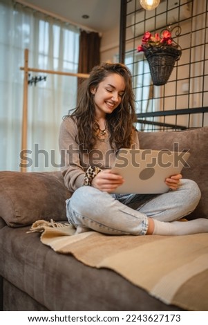 A young girl studying or doing business from her home while sitting on sofa and working on her laptop and drinking coffee during the day