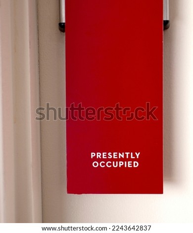 Red sign hanging on door that says Presently Occupied