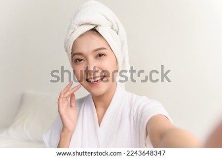 POV selfie photo of young beautiful Asian woman taking care of her facial skin after apply face skin care cosmetic lotion moisturizer product and checking in mirror at home. Woman beauty care concept