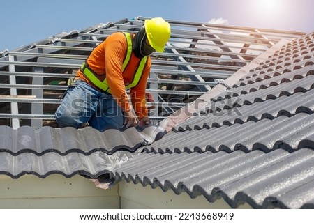 Roof repair, worker replacing gray tiles or shingles on house with blue sky as background and copy space, Roofing - construction worker standing on a roof covering it with tiles. Royalty-Free Stock Photo #2243668949