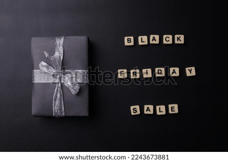 Black friday sale word arrange with gift box using silver ribbon on black background. 
